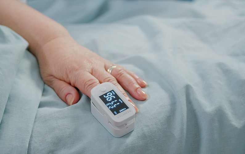close-up-of-oximeter-on-hand-of-senior-patient-laying-in-bed-aged-person-having-electronic-device-for-oxygen-saturation-and-pulse-pressure-measurement-on-finge