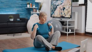 Aged person lifting weights with dumbbells and watching video
